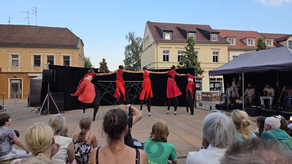Bild vergr&ouml;&szlig;ern: Foto: Menschen beobachten ein Theaterstück mit fünf rotgekleideten Personen auf Stelzen.