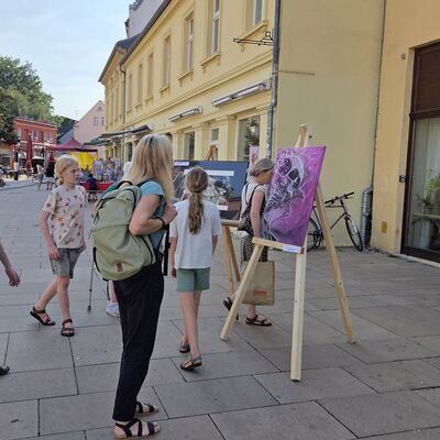 Bild vergr&ouml;&szlig;ern: Foto: Menschen zwischen Staffeleien mit Kunstwerken.