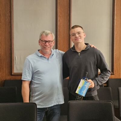 Foto: Zwei Männer vor einer getäfelten Wand.