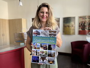 Bild vergr&ouml;&szlig;ern: Eine Frau hält einen Kalender und lächelt in die Kamera.