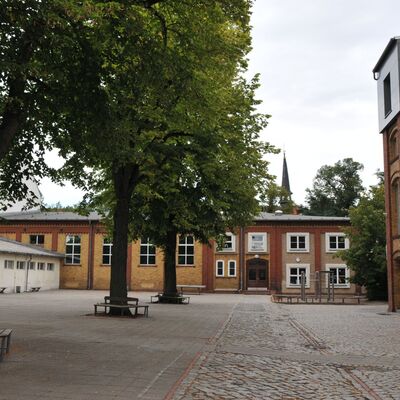 Bild vergr&ouml;&szlig;ern: Foto: Mehrere Gebäude um einen gepflasterten Hof mit Bäumen.