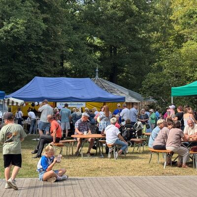 Bild vergr&ouml;&szlig;ern: Viele Menschen stehen an Zelten oder sitzen an Tischen.