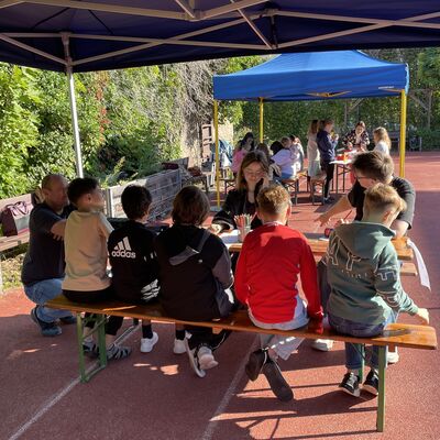 Bild vergr&ouml;&szlig;ern: Foto: Kinder und Erwachsene sitzen auf Bänken.