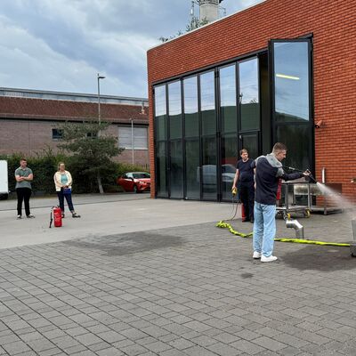 Bild vergr&ouml;&szlig;ern: Ein junger Mann löscht ein simuliertes Feuer, während andere Personen zuschauen.