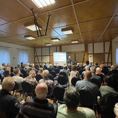 Foto: Ein Raum voller Menschen. Vorne steht ein Mann an einer Leinwand.