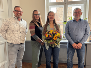 Bild vergr&ouml;&szlig;ern: Zwei Männer und zwei Frauen stehen nebeneinander und lächeln. Eine Frau hält einen Blumenstrauß.