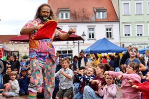 Bild vergr&ouml;&szlig;ern: Auf einer Bühne steht ein bunt bemalter Mann. Vor der Bühne sind Kinder, die zu ihm sehen.