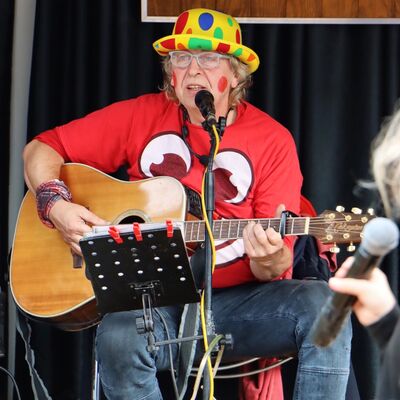 Bild vergr&ouml;&szlig;ern: Ein Mann sitzt in bunten Sachen mit einer Gitarre auf einer Bühne.