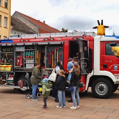 Bild vergr&ouml;&szlig;ern: Eltern und Kinder stehen an einem Feuerwehrauto und lasse sich das Fahrzeug zeigen.