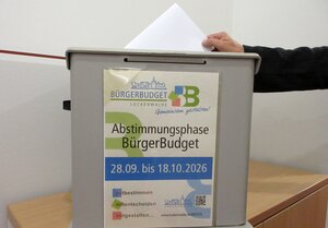 Bild vergr&ouml;&szlig;ern: Eine Wahlurne beklebt mit einem Plakat "Abstimmungsphase BürgerBudget", 28.09. bis 18.10.2026.