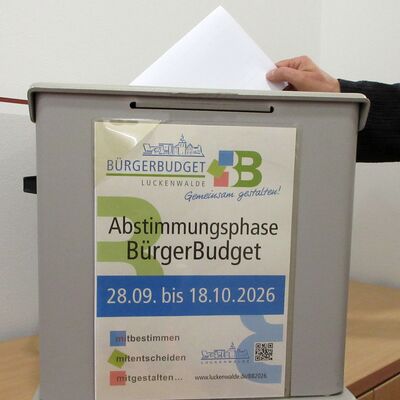 Eine Wahlurne beklebt mit einem Plakat "Abstimmungsphase BürgerBudget", 28.09. bis 18.10.2026.