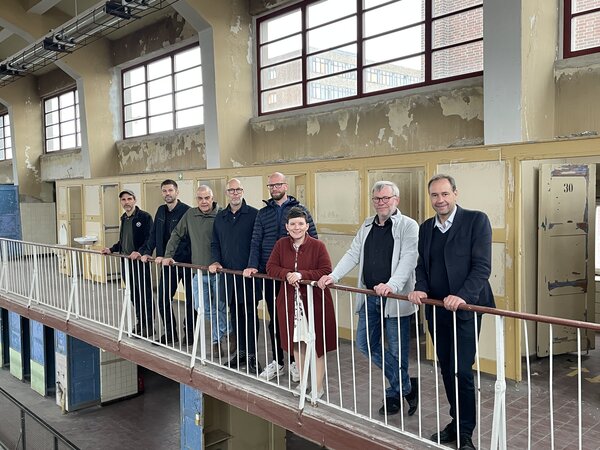 Bild vergr&ouml;&szlig;ern: Foto: Eine Gruppe Menschen hinter einem Geländer in einem unsanierten Gebäude.