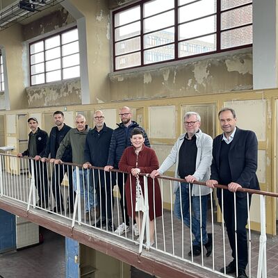 Foto: Eine Gruppe Menschen hinter einem Geländer in einem unsanierten Gebäude.