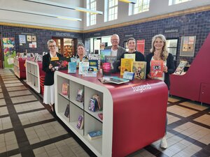 Bild vergr&ouml;&szlig;ern: Foto: Vier Frauen und ein Mann stehen in einer großen Halle hinter einem weiß-roten Regal mit Büchern.