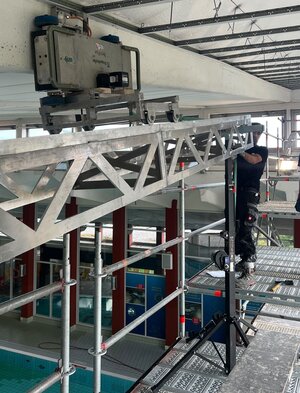Bild vergr&ouml;&szlig;ern: Auf einem Gerüst befindet sich ein Mann, der Untersuchungen an der Decke einer Schwimmhalle vornimmt.