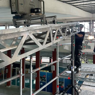 Auf einem Gerüst befindet sich ein Mann, der Untersuchungen an der Decke einer Schwimmhalle vornimmt.