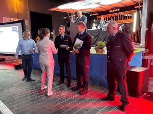 Bild vergr&ouml;&szlig;ern: Vor einer Bühne stehen Feuerwehrleute und bekommen Urkunden überreicht.