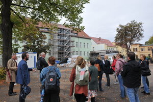 Bild vergr&ouml;&szlig;ern: Foto: Eine Gruppe Menschen vor einem Gebäude mit Gerüst.
