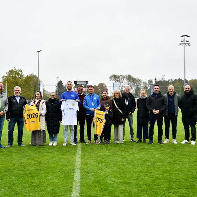 Mehrere Menschen stehen auf einem Fußballplatz und lächeln in die Kamera.