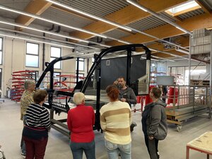 Bild vergr&ouml;&szlig;ern: Foto: Menschen stehen vor einem schwarzen Metallgehäuse in einer großen Halle.